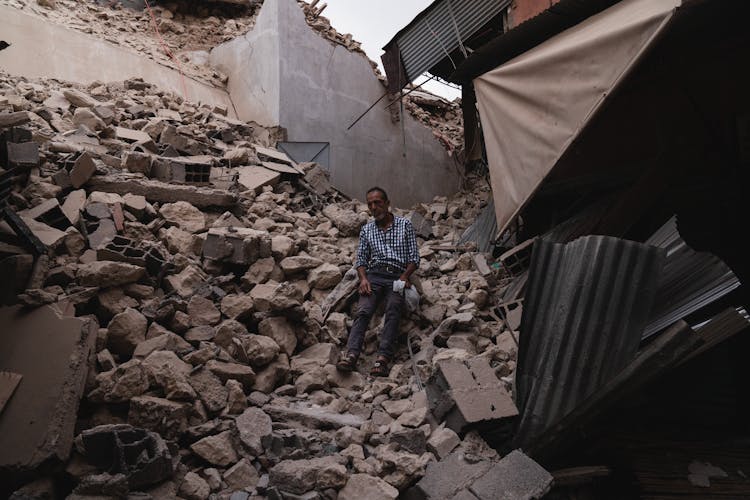 Man Sitting Amid Rubble Of A Destroyed House