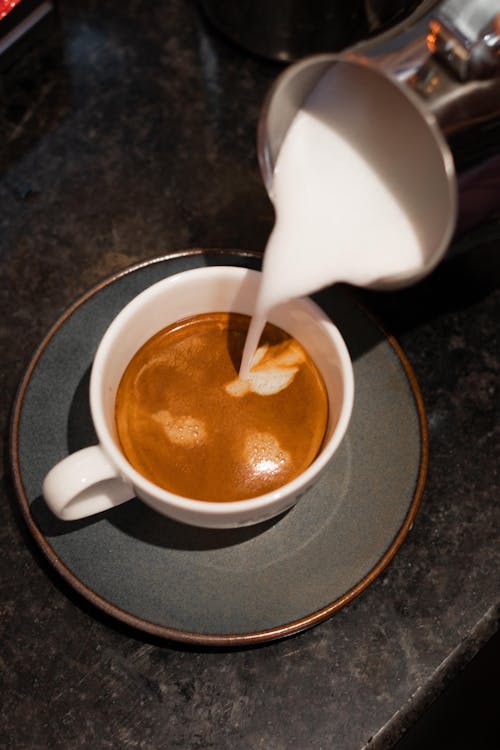 Pouring Milk Into a Cup of Coffee on a Saucer