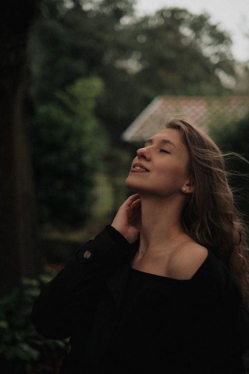 Free Portrait of a woman with eyes closed savoring the breeze in a lush rural landscape. Stock Photo