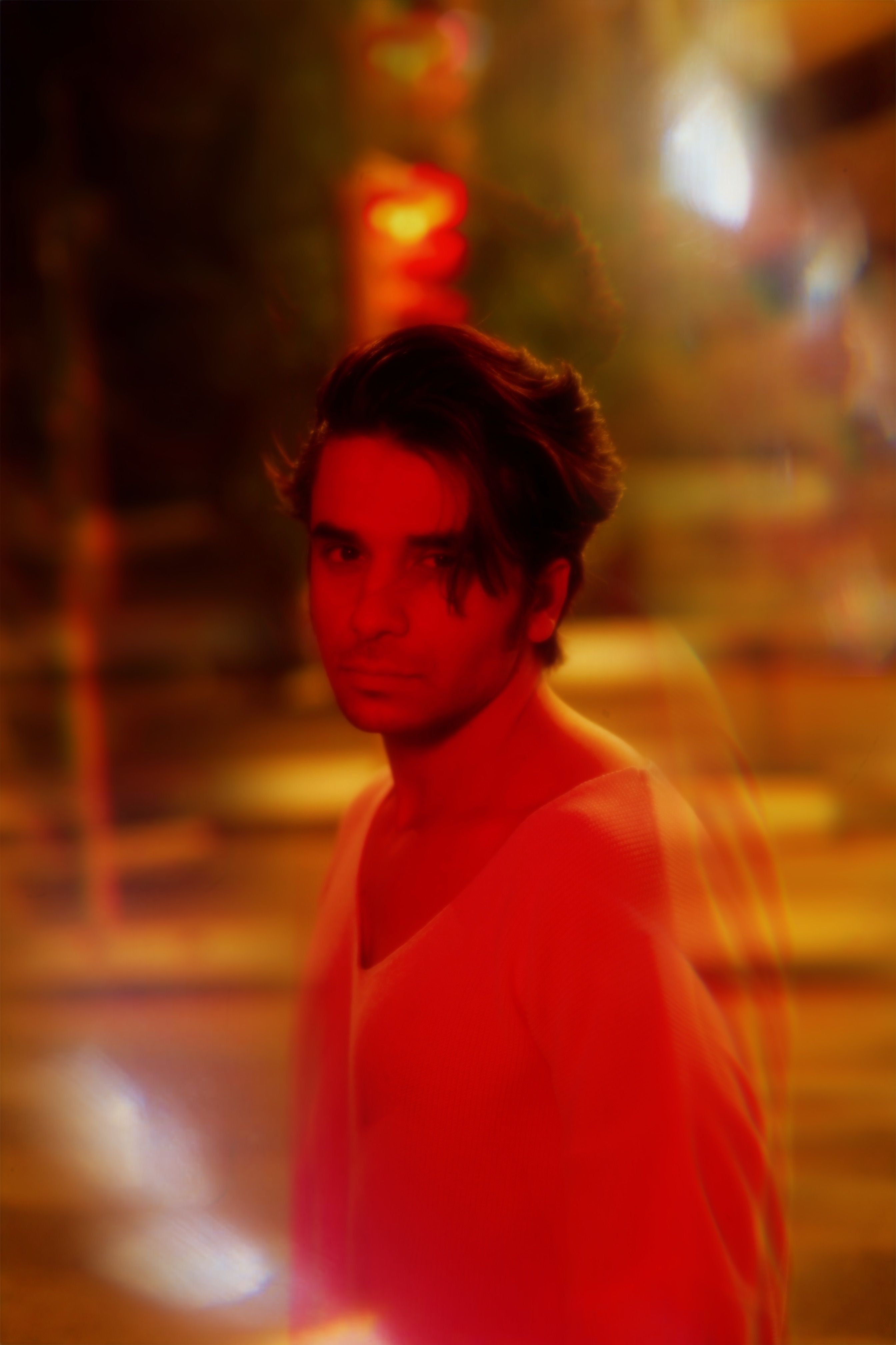 A blurred portrait of a man under red light on urban streets at night.