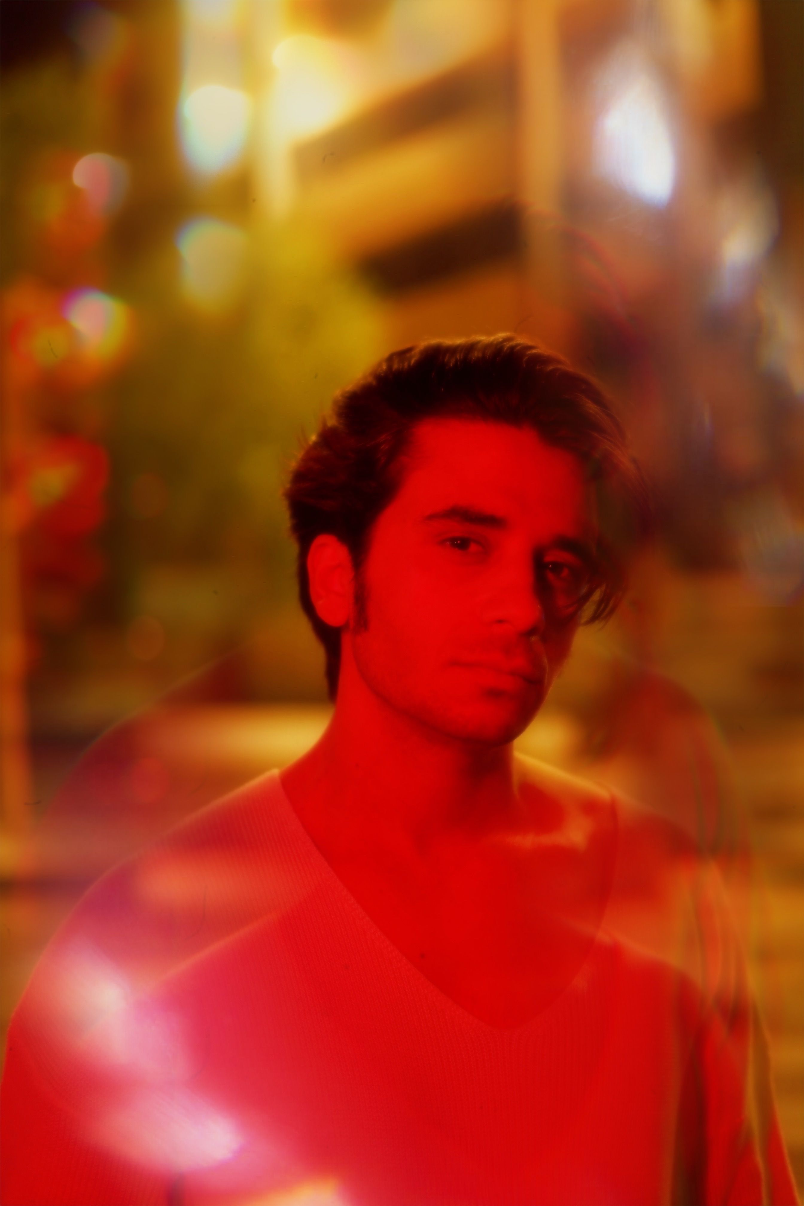 A man standing on a city street at night, bathed in red light. Artful and moody.