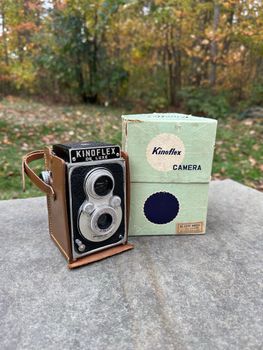 A vintage Kinoflex camera with its original box featured outside on a stone surface.