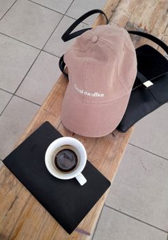 A pink baseball cap, coffee mug, and notebook on a wooden bench convey a relaxed, out-of-office vibe.