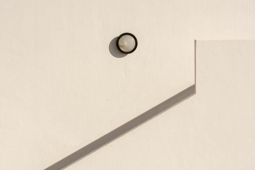 Geometric shadows and minimalist design featuring a circular wall lamp and angled shadows on a white background.