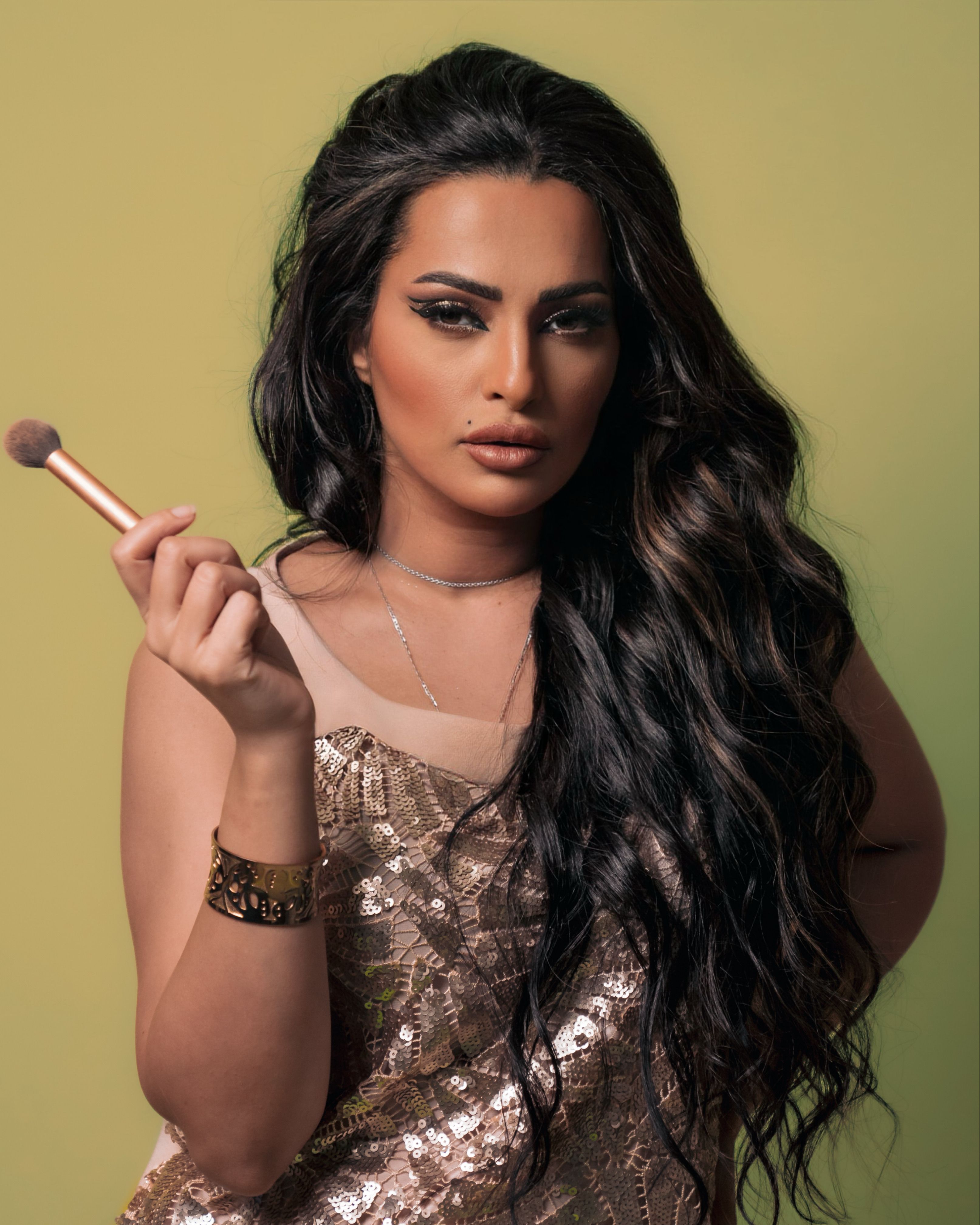 Glamorous woman with long hair holding a makeup brush against a yellow background.