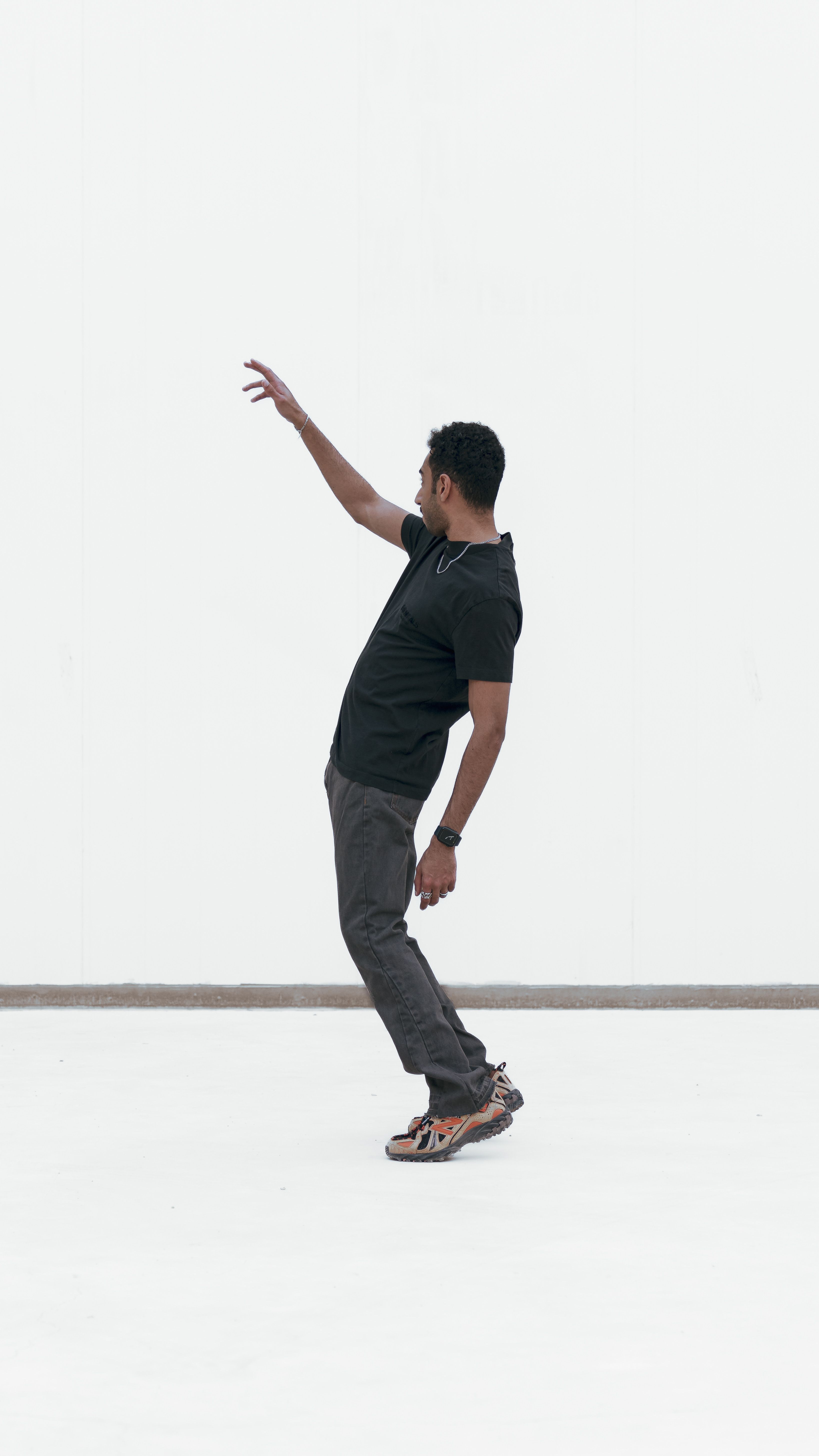 A man in casual clothing poses dynamically in a studio with a white background.
