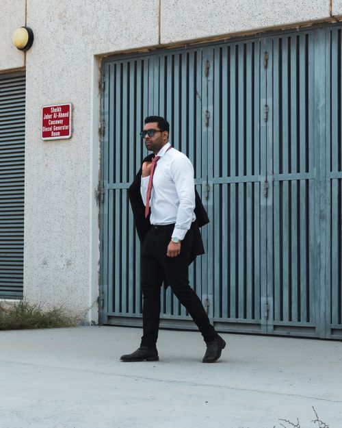Free Young businessman in formal attire walking confidently outdoors with sunglasses and a suit jacket. Stock Photo