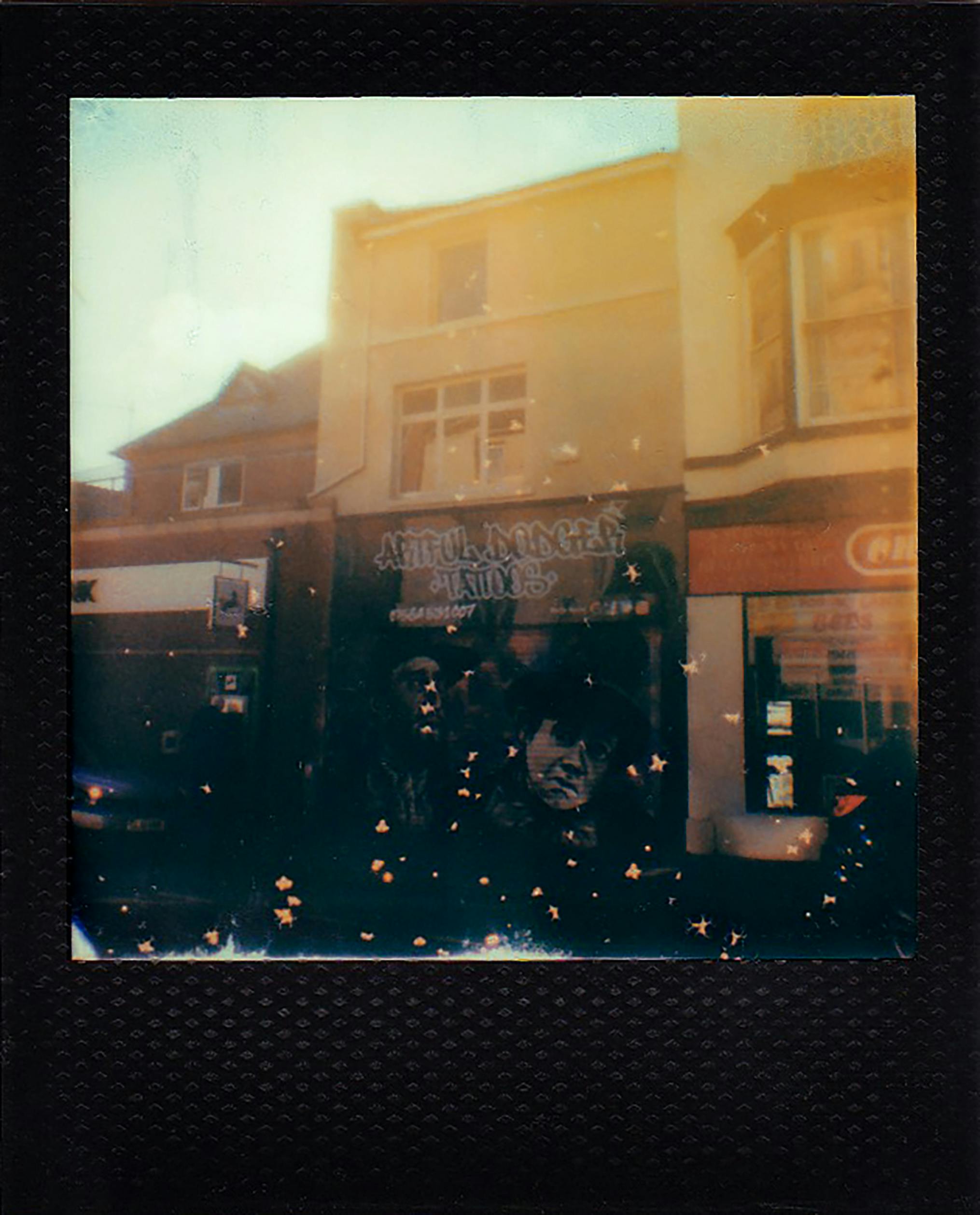 Vintage Polaroid capturing a city street mural at a tattoo parlor, with a nostalgic urban vibe.