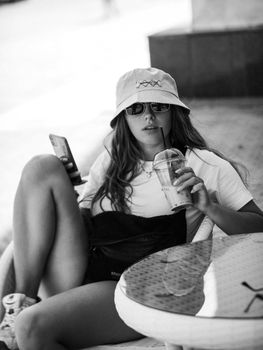 Young woman in a bucket hat sipping a cold drink outdoors, exuding relaxed style.