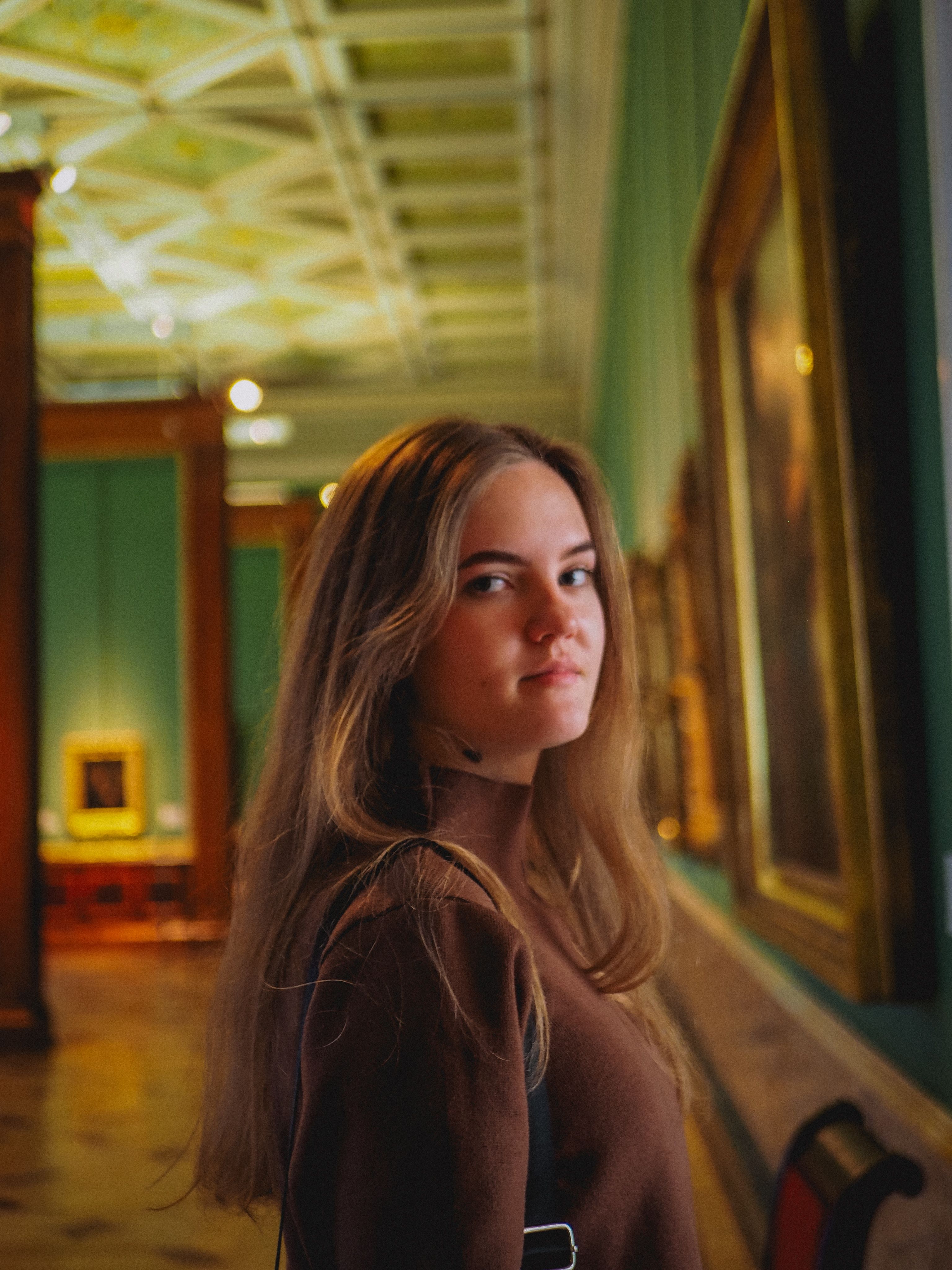 A woman in a brown turtleneck sweater observes art in a museum gallery.