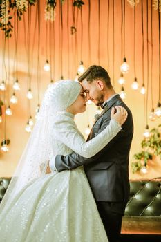 Elegant bride and groom embracing under hanging lights during a wedding ceremony.