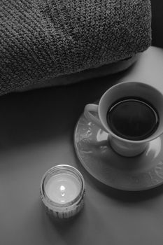 A serene, cozy setup featuring candlelight, a coffee cup, and a knit blanket.