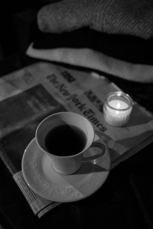 Free Black and white image of a cozy morning setup with coffee, newspaper, and candlelight. Stock Photo