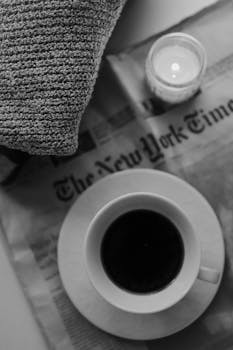 A black coffee cup and candle on a newspaper, perfect for a cozy morning.