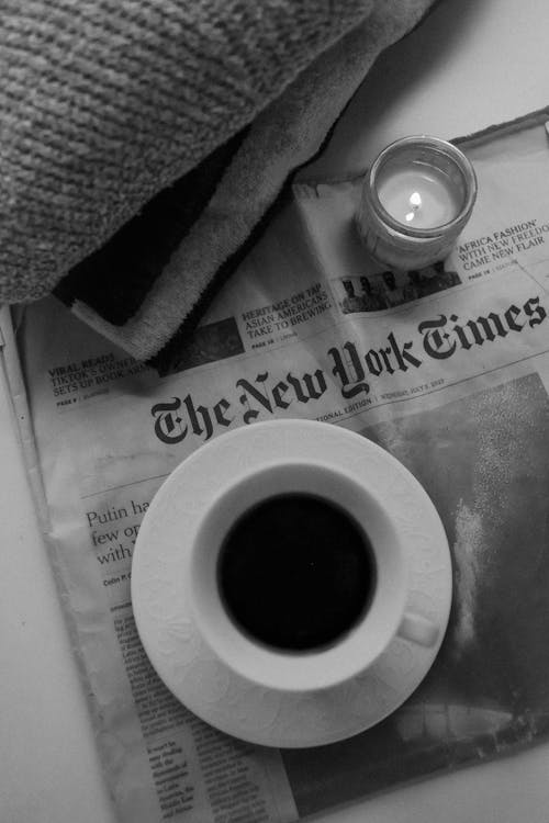 Free Cup of Coffee and Burning Candle Standing on The New York Times Newspaper Stock Photo