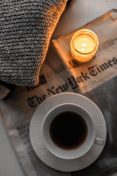A warm scene of coffee, candlelight, and a newspaper on a cozy morning.