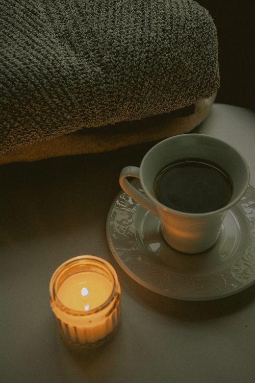 Free A cozy scene with a burning candle, a cup of coffee, and woolen fabrics on a table. Stock Photo