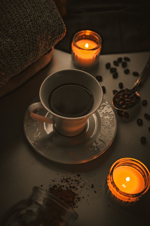 Free A warm, inviting scene featuring a coffee cup surrounded by candles and coffee beans on a table. Stock Photo