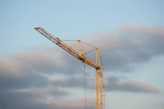 A towering yellow crane set against a backdrop of blue sky and clouds, symbolizing construction and industry.