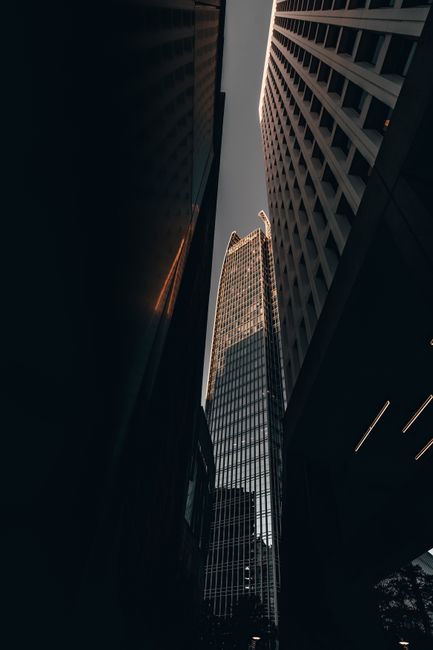 A towering skyscraper in a modern cityscape illuminated by striking light and shadows.