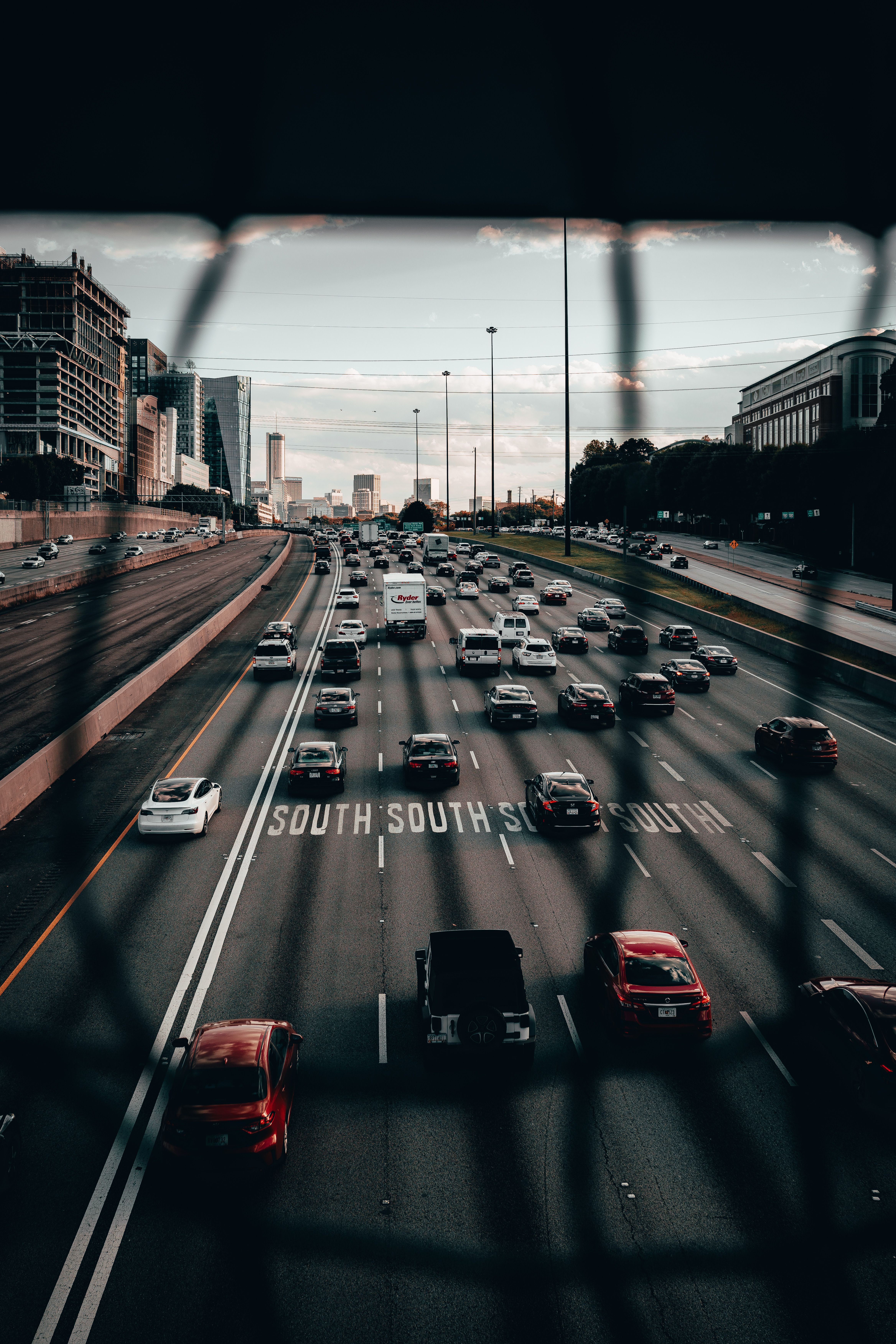 View of a busy multi-lane highway with city buildings in the background during evening rush hour.