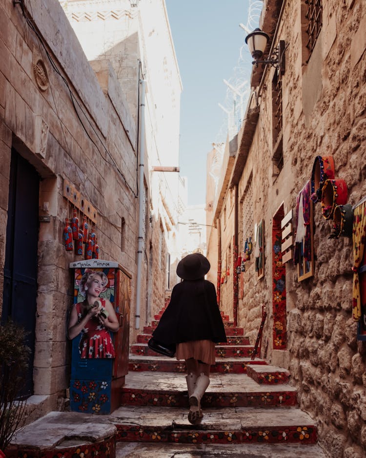 Woman In Black Blazer And Wide-Brimmed Hat Walking Up Steps On A Narrow Old Town Alley