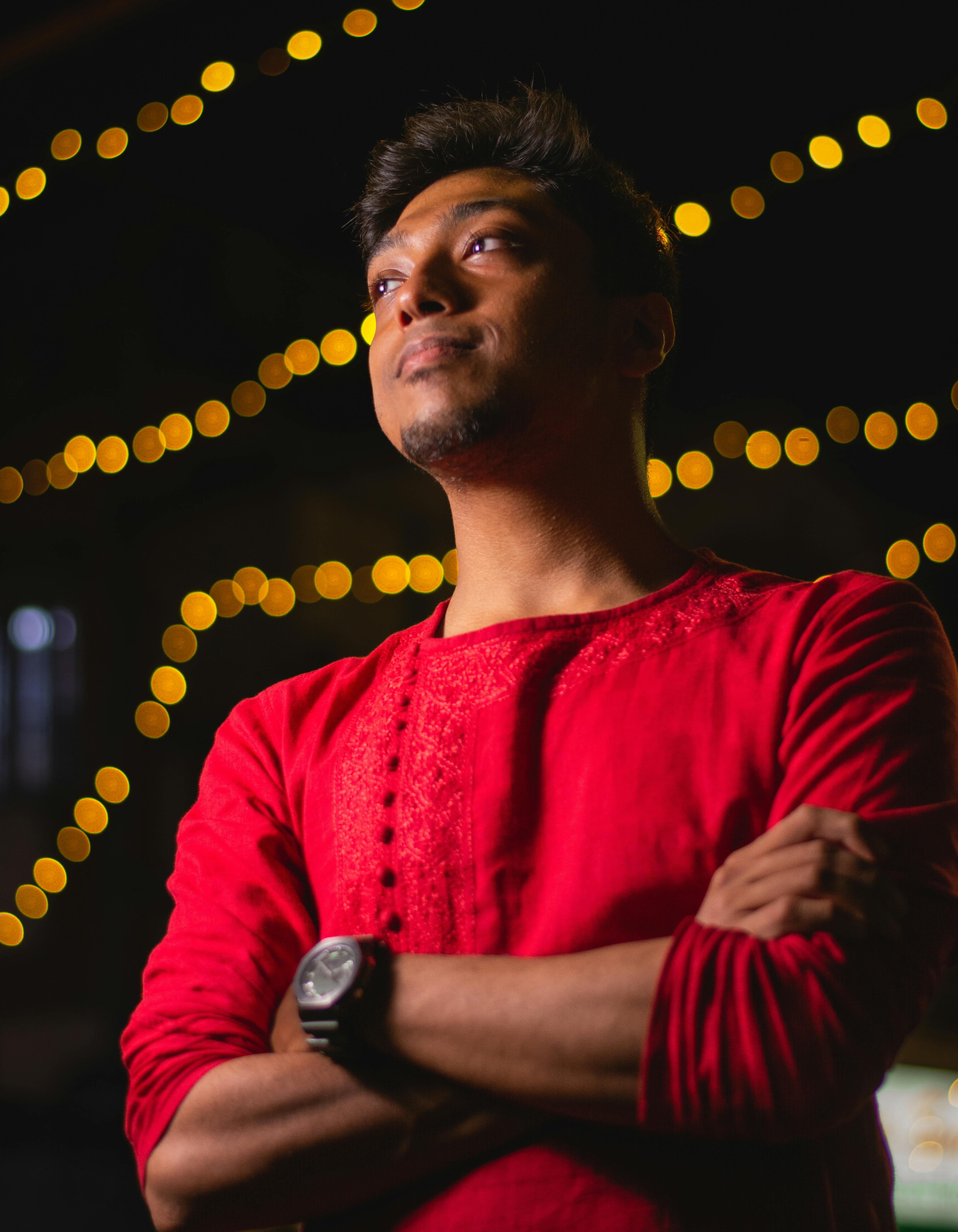 Portrait of a man in a red sweater enjoying a vibrant night setting with string lights.