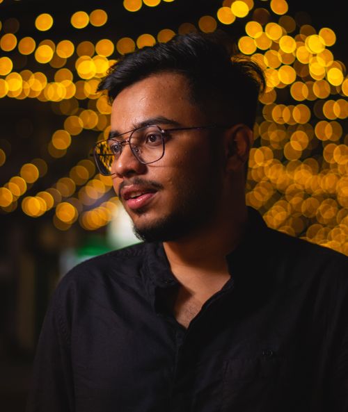 Free Young man with eyeglasses posing against vibrant bokeh lights at night. Stock Photo