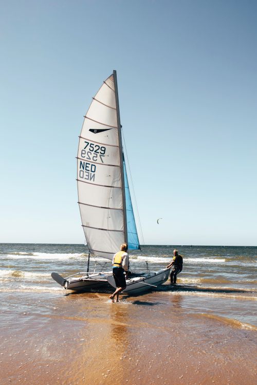 Free Two adults prepare a sailboat on Noordwijk beach, perfect summer day for adventure. Stock Photo
