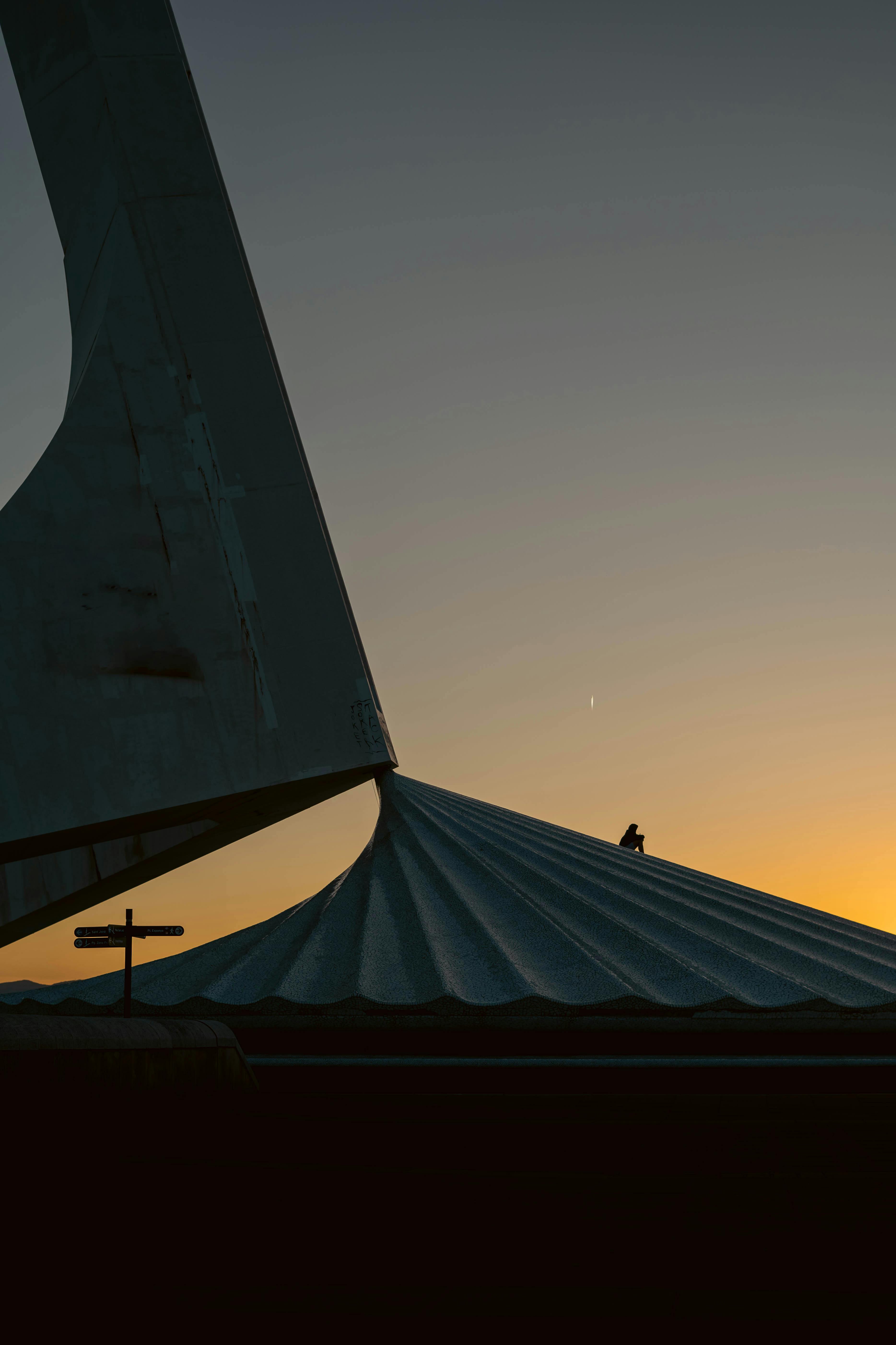 Silhouette of a modern sculpture against a sunset sky in Barcelona, Spain. Unique architectural shapes create an artistic scene.