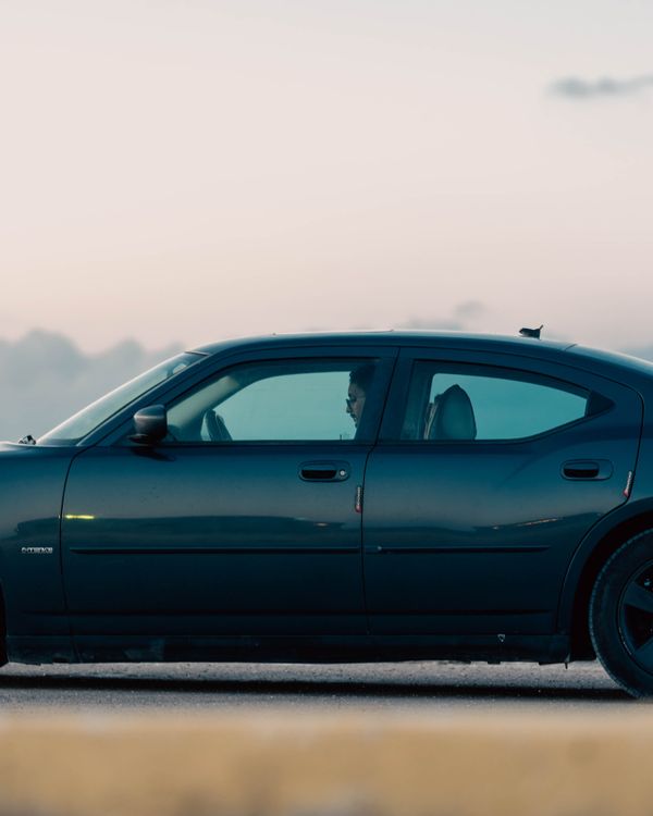 A sleek car parked by a coastal road in Libya during dawn, creating a serene scene.