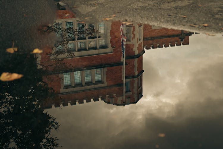 Reflection Of Building And Flag In Puddle