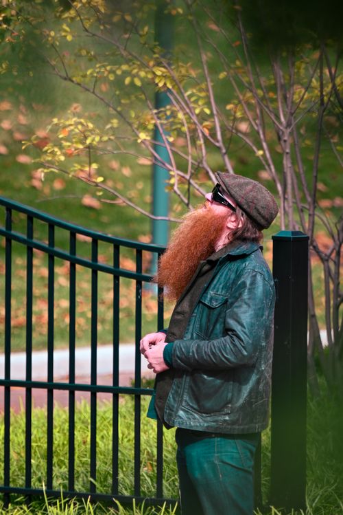Free A redheaded man with a beard in a leather jacket looks up thoughtfully outdoors. Stock Photo