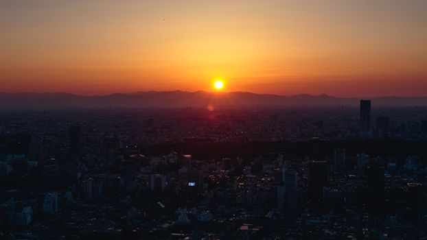 Breathtaking sunrise over Tokyo cityscape with vibrant orange and yellow hues illuminating the skyline.