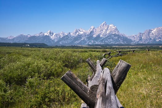 Idyllic rural landscape with rustic wooden fence and stunning mountain range view under clear blue skies.