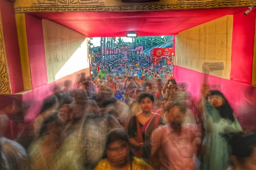 Blurred motion captures a bustling festival crowd in Kolkata, India, through a colorful passageway.