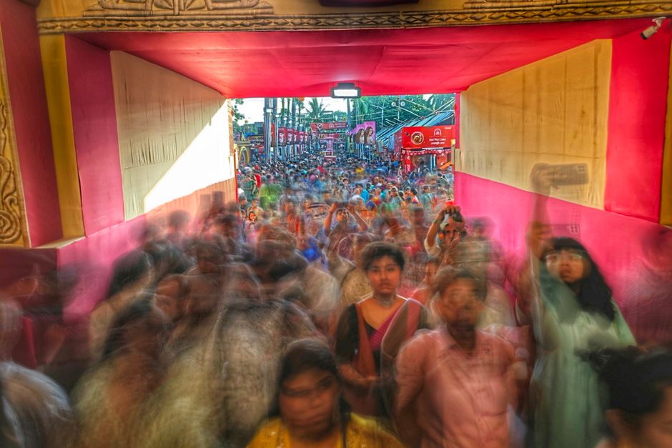 Blurred motion captures a bustling festival crowd in Kolkata, India, through a colorful passageway.