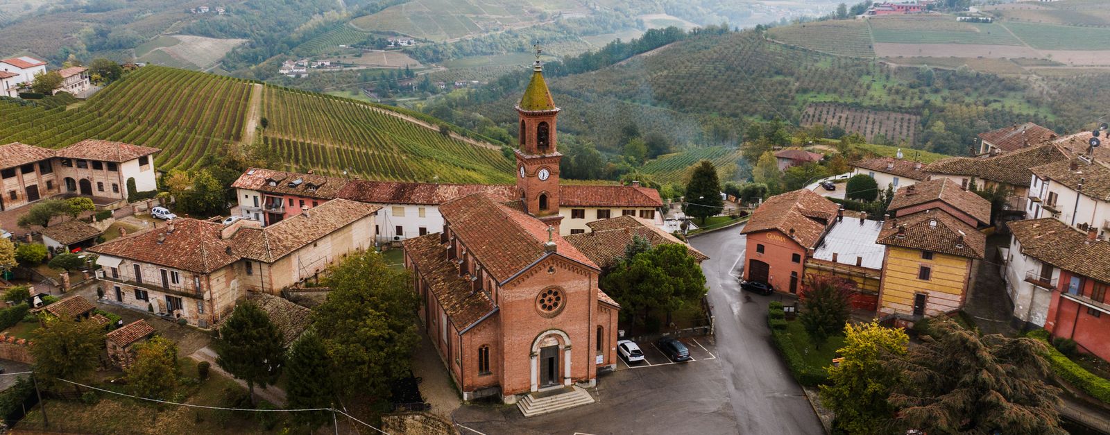 A picturesque aerial view of a traditional village in Piedmont, Italy, surrounded by lush vineyards.