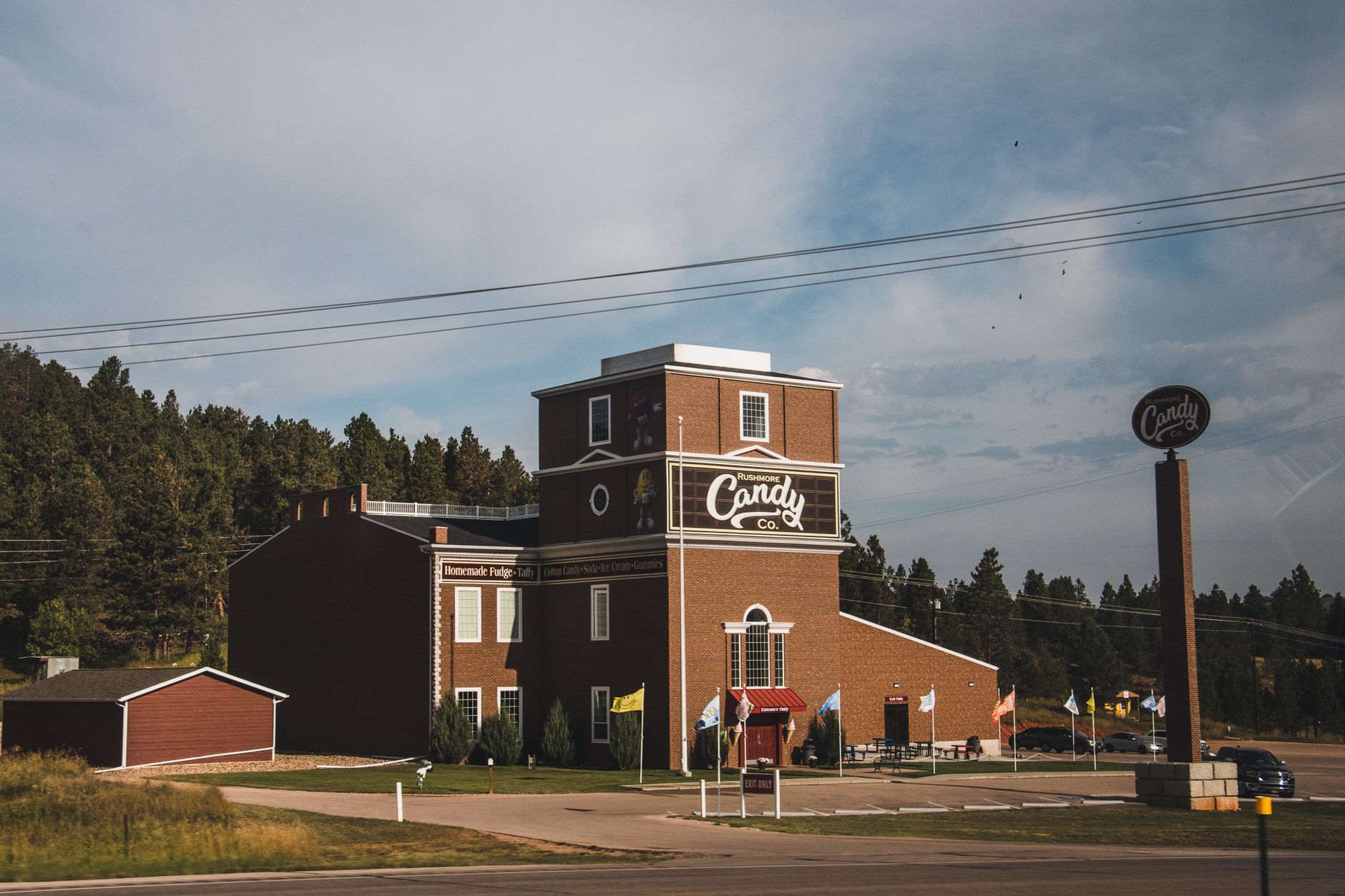 A daylight view of the Rushmore Candy Co. building surrounded by trees, featuring a small driveway.