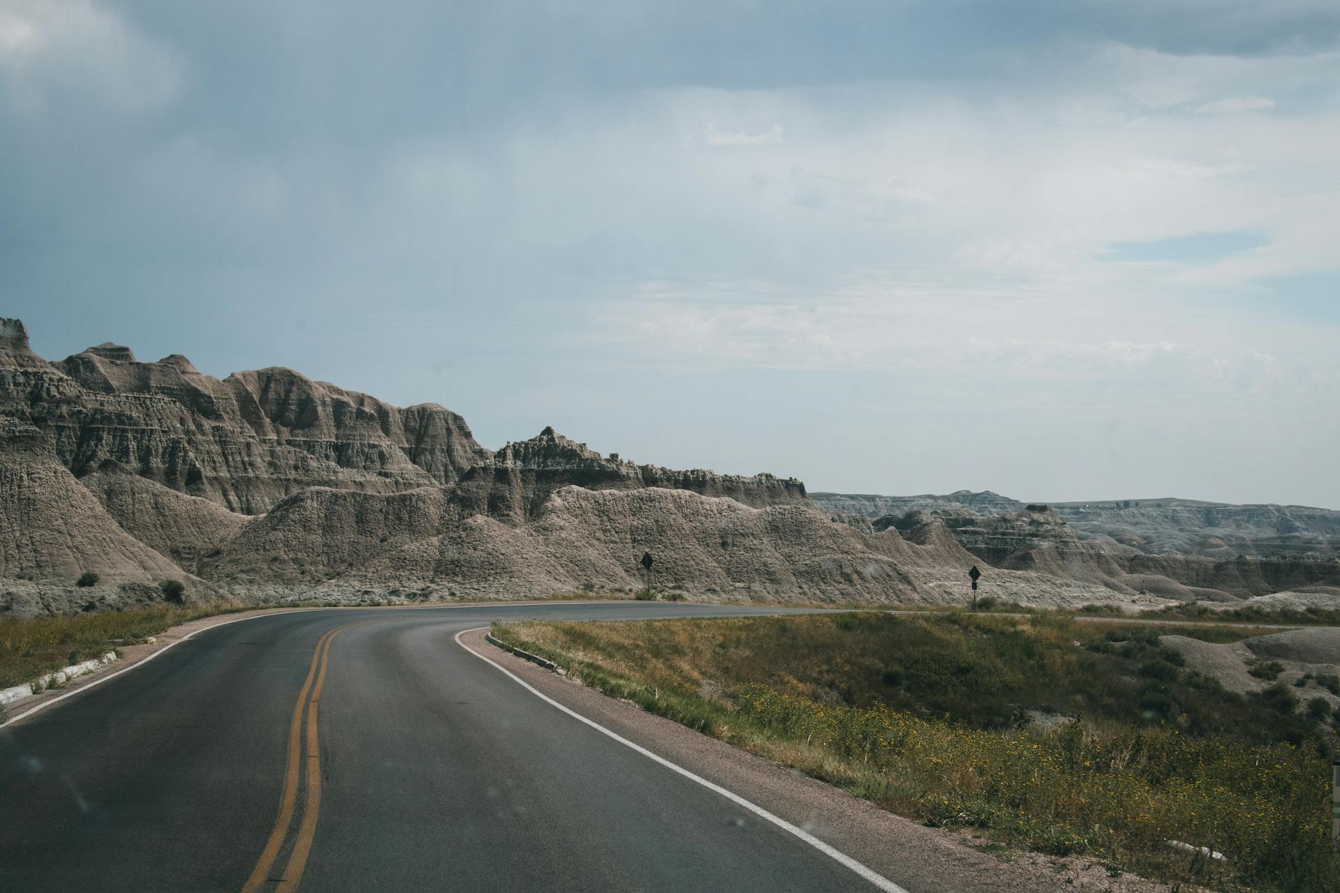 Empty highway curving through the rugged landscapes of Badlands National Park under a cloudy sky.