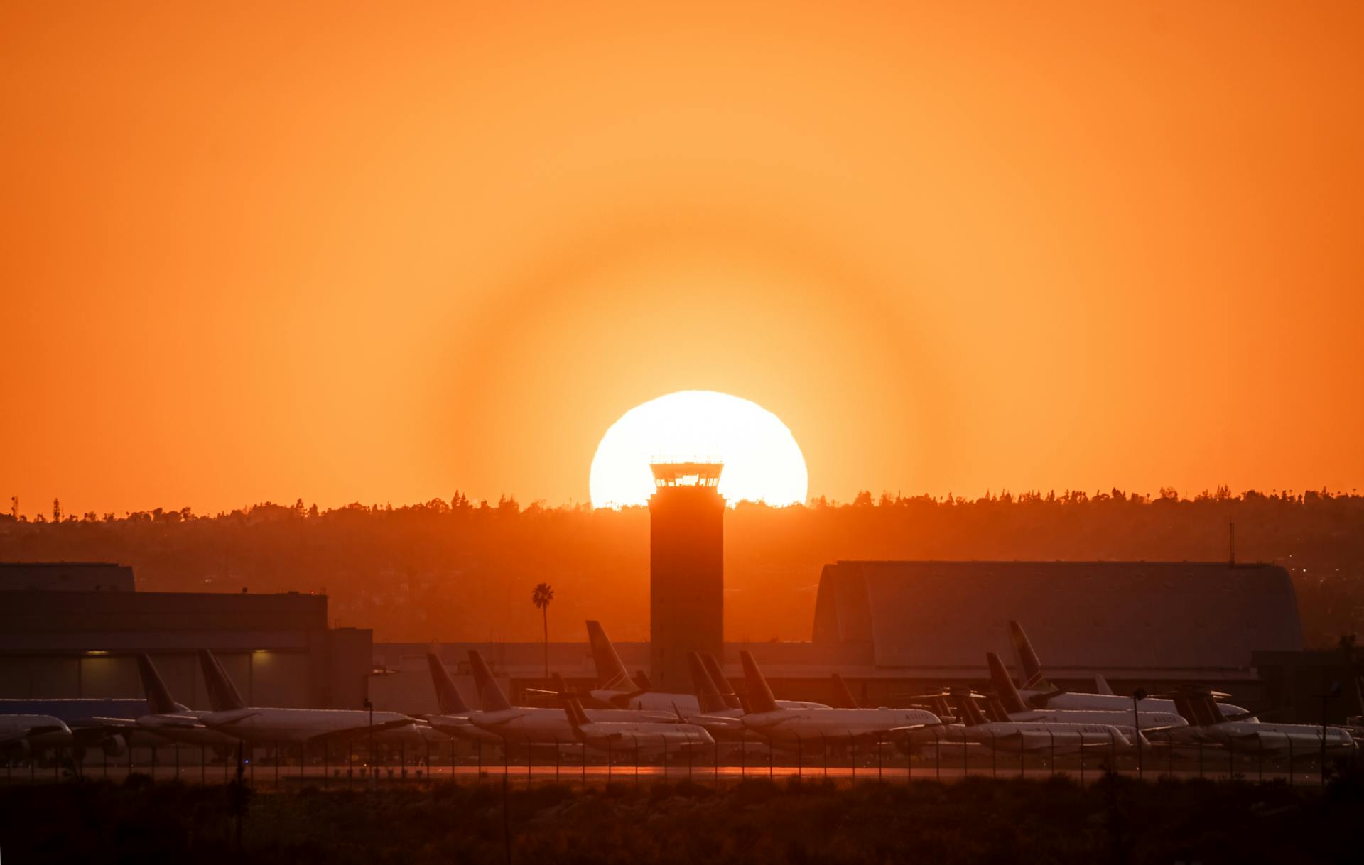 Vibrant sunset at San Bernardino Airport with airplanes and air traffic control tower silhouetted against the orange horizon.