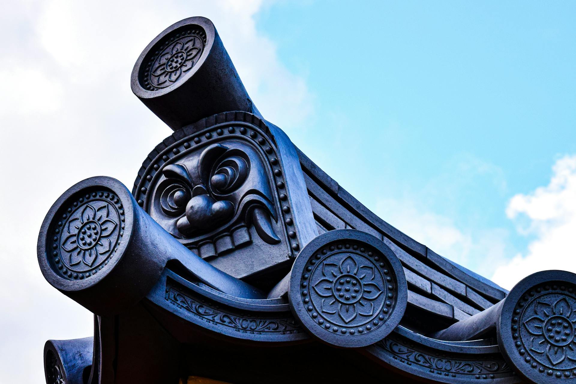 Close-up of Japanese onigawara tile with intricate carvings on a temple roof against a blue sky.