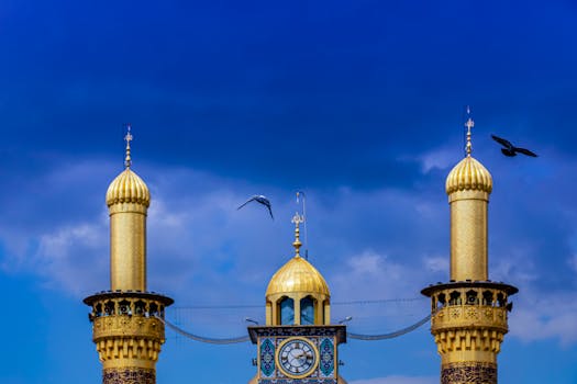 Beautiful view of the Karbala mosque's golden minarets against a dramatic summer sky with birds flying.