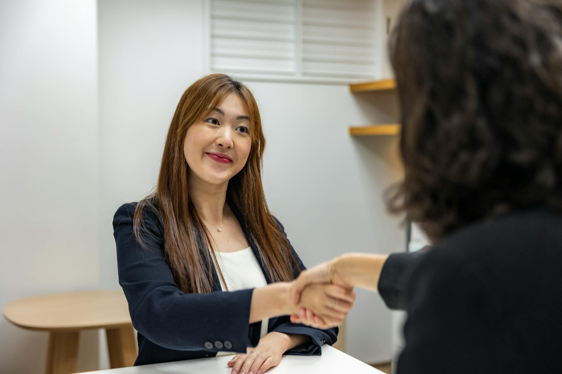 Businesswoman in professional attire shaking hands with recruiter in an office setting.