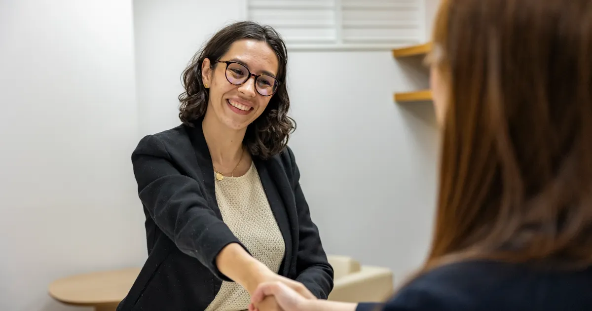 Two women shaking hands across a desk in an office, representing OpenAI DOJ PERM settlement hiring discrimination vendor risk