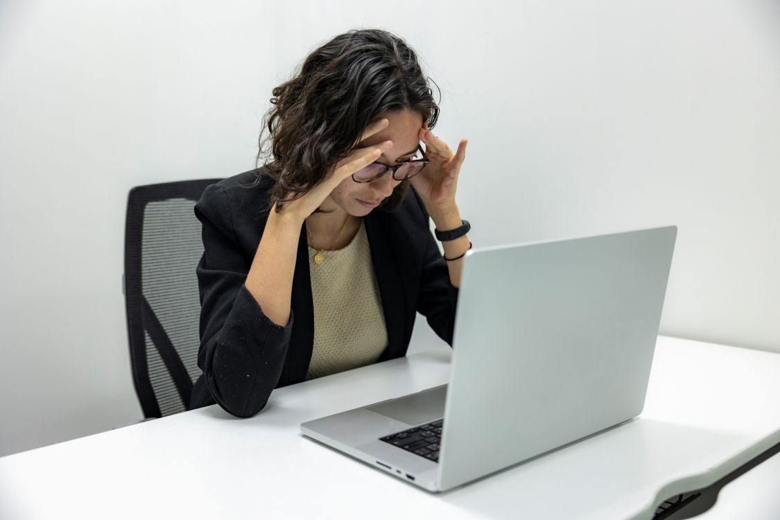 Zmęczona pracownica z bólem głowy przy laptopie po wielu godzinach pracy przy monitorze.