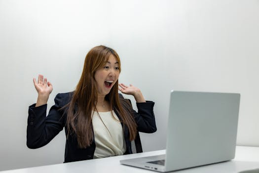 A joyful businesswoman expresses excitement while working on her laptop in a modern office.