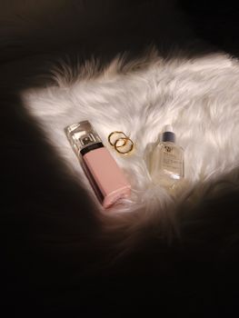 Elegant display of perfume and jewelry on soft fur with dramatic lighting.