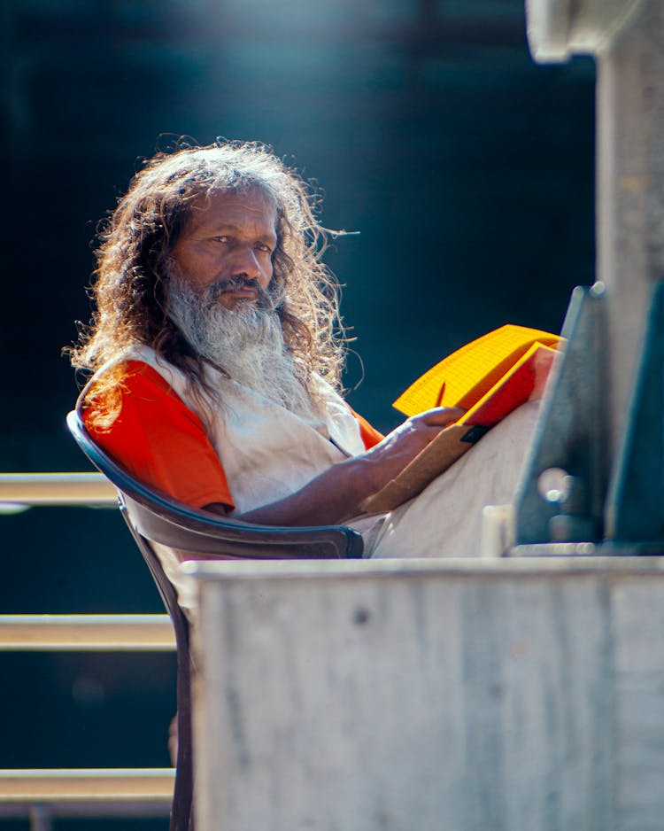 Elderly Man With A Gray Beard Sitting On A Chair Outside 