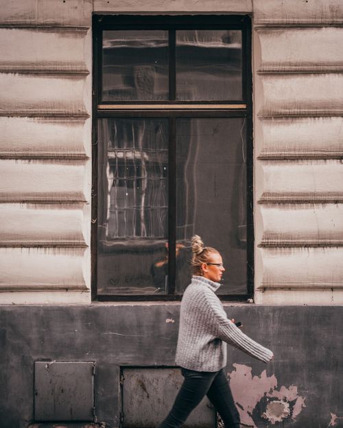 Free Woman with glasses and blonde hair walking past a city building in autumn. Stock Photo